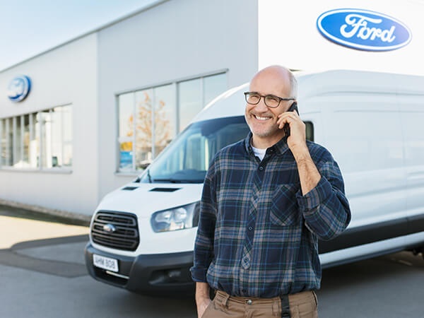Mann steht vor einem Ford-Transporter und telefoniert, lächelt freundlich.